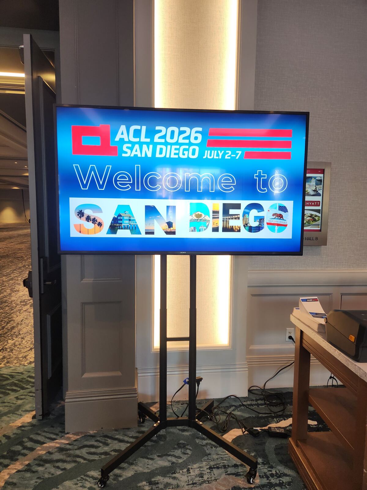A screen inside the venue welcoming visitors to ACL 2026 San Diego, July 2-7, beside the registration desk.
