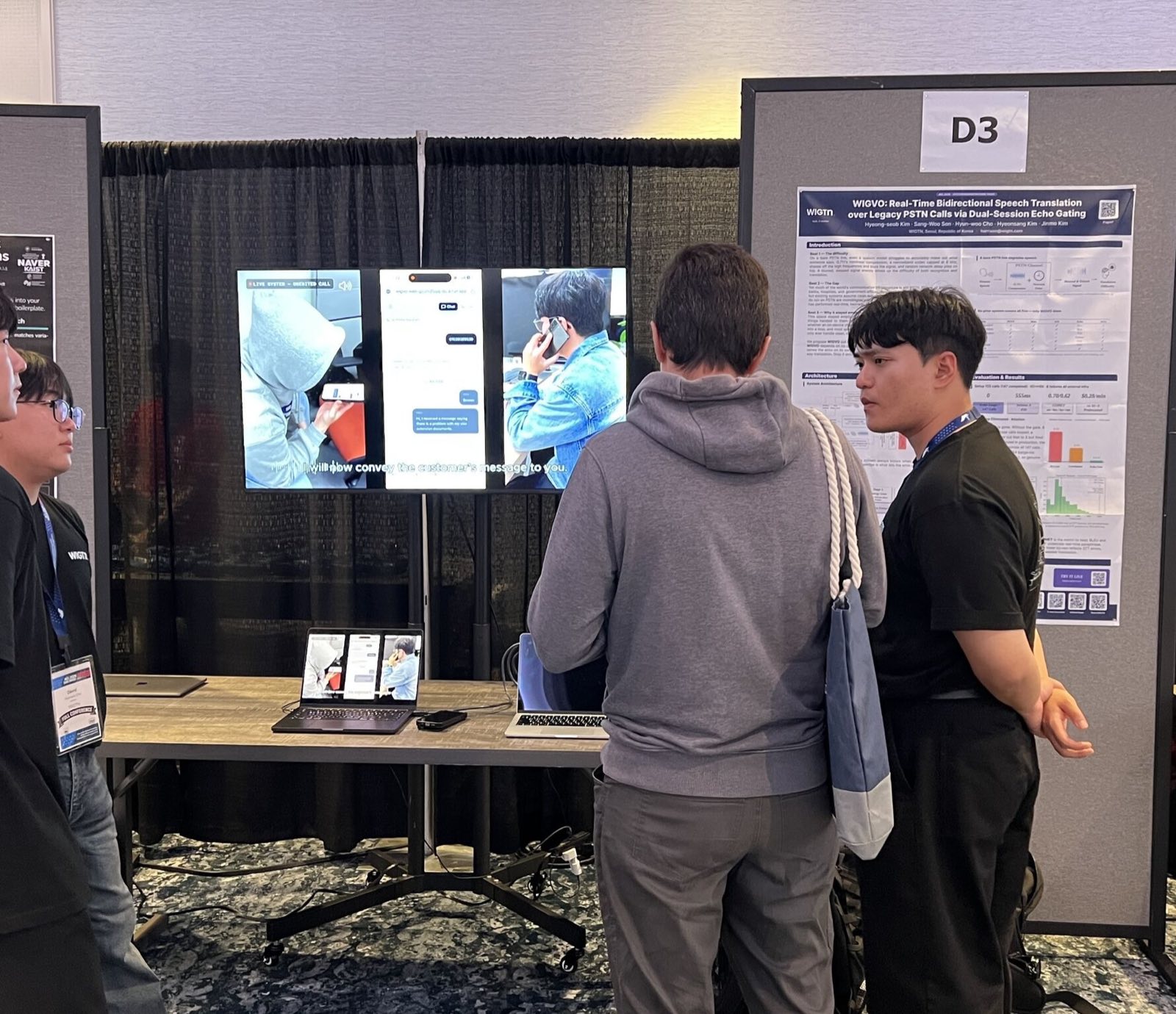 The WIGTN booth at ACL 2026: the WIGVO poster on the right, three screens showing a live call in progress, and visitors talking with the team.