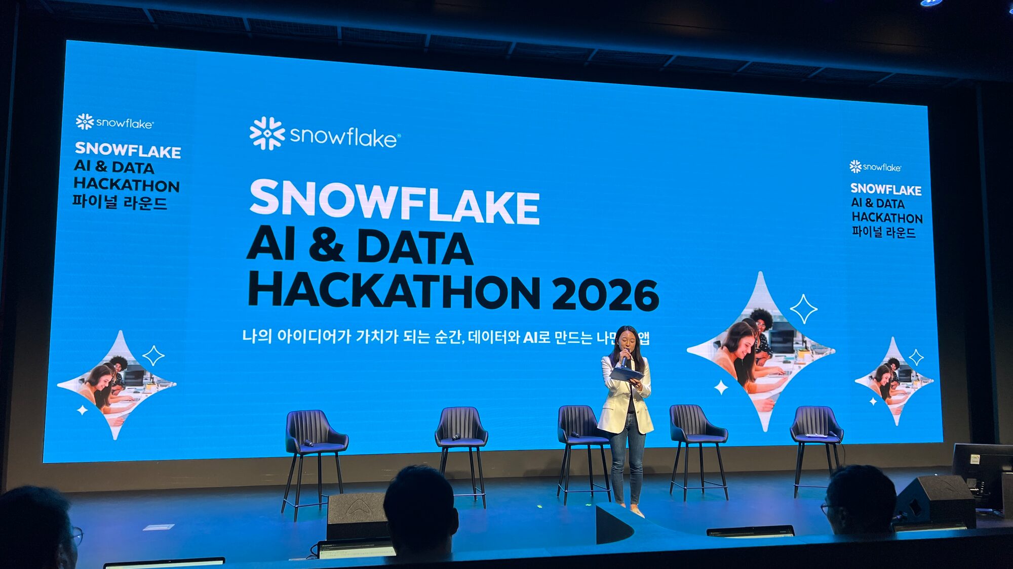 The Snowflake AI & Data Hackathon 2026 final round stage in Seoul, with the event banner filling the screen behind five empty chairs and a host at the microphone.
