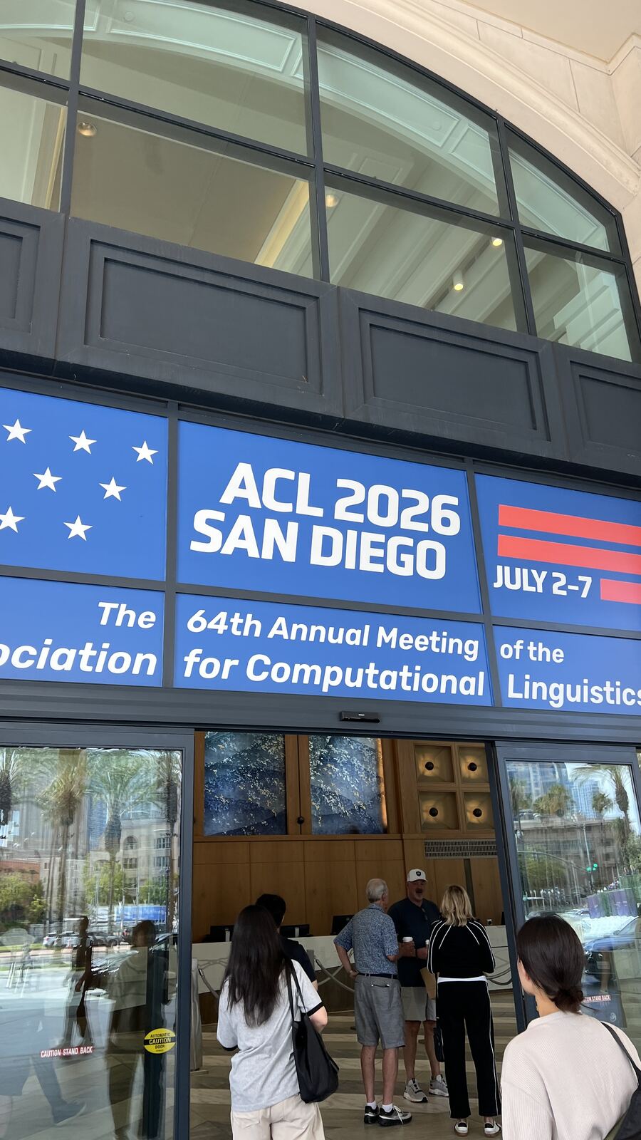 The ACL 2026 San Diego banner across the glass frontage of the convention centre, with attendees queueing at registration inside.
